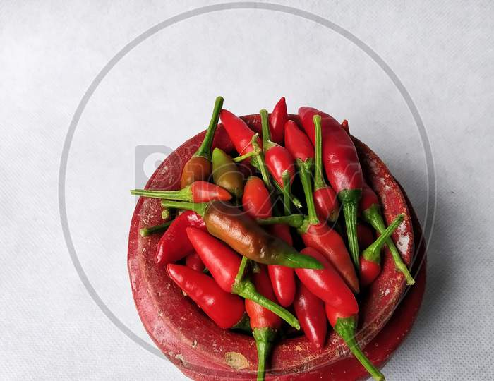 Red Chilli In A Red Colored Crock (Mud Made Pot) In A White Background