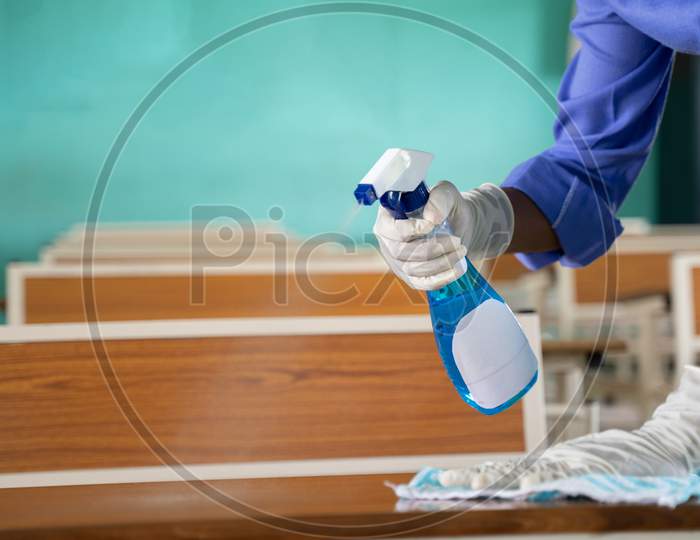 Close Up Of Hands With Gloves Disinfecting Desk By Using Sanitizer At Classroom - Cleaning Dust On Table Surface With Cloth And Disinfectant Spray To Protect From Coronavirus Or Covid-19 Infection.