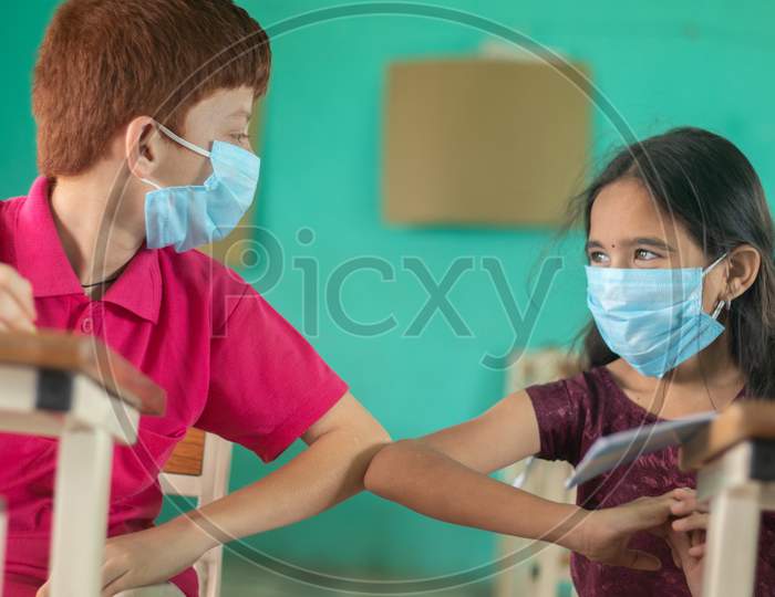 Two Kid In Medical Mask At Classroom Greeting Each Other With Elbow Bumps While Maintaining Socail Distance At School - Concept Of School Reopen, Back To School Safety Measures And New Normal Lifestye