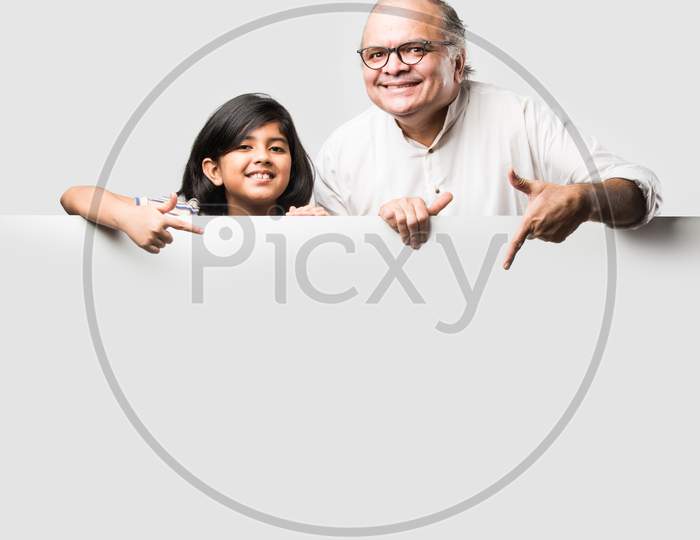 Indian Asian Cute Little Girl Pointing At Blank White Board With Grandpa Or Grandfather