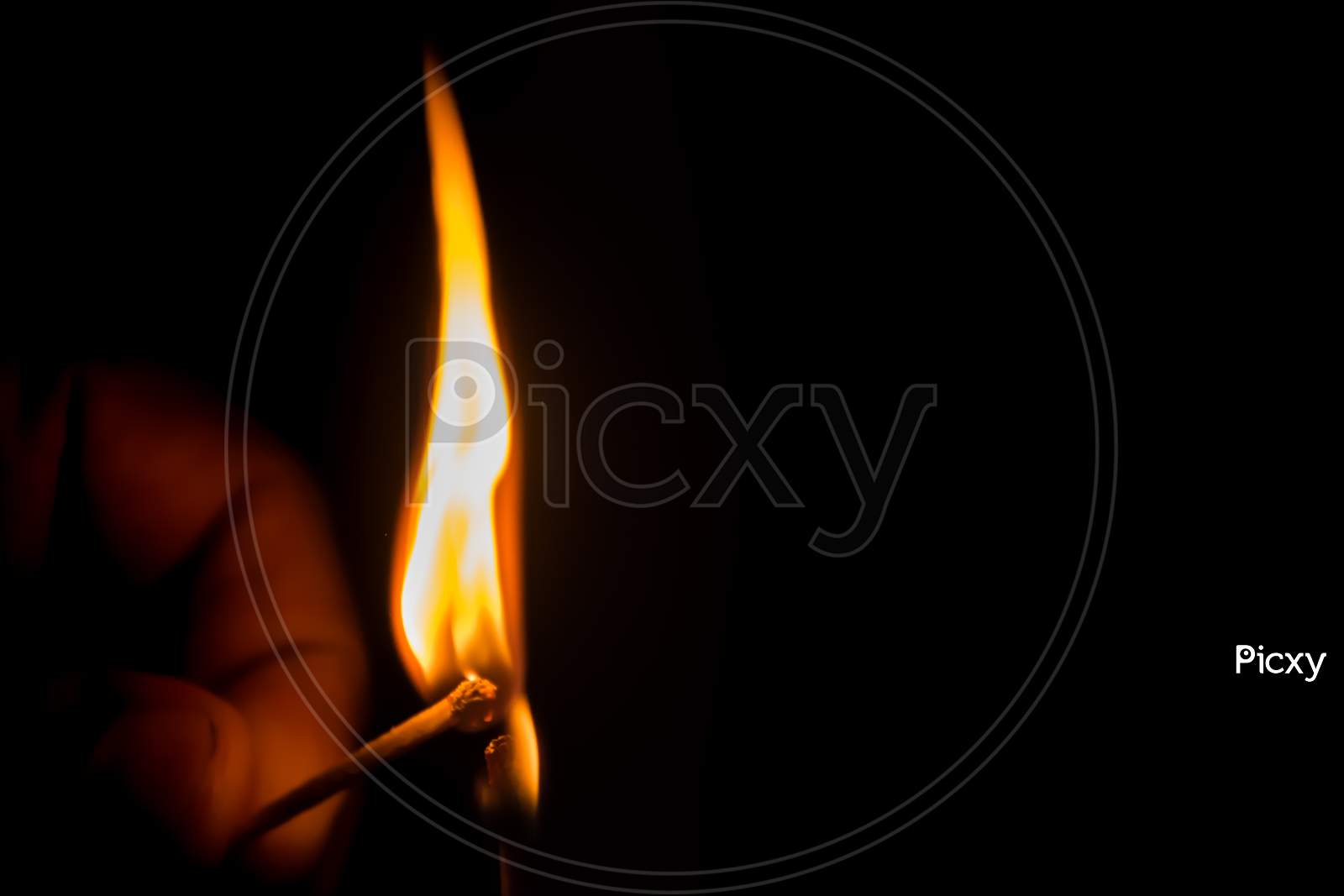 Close-Up Of A Burning Matchstick Held In A Hand On A Black Background