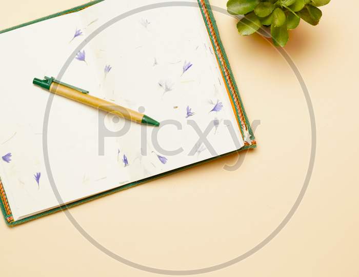 Top View Of Notebook With Pen And Plant Workspace. Flat Lay