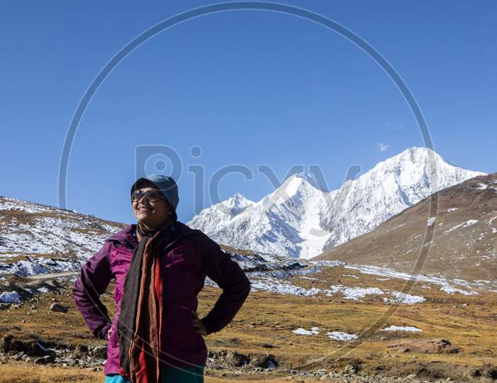 A Young Lady With Red Jacket On The Top Of Kunzum Pass In Front Of Snow Peaks On The Himalays In India