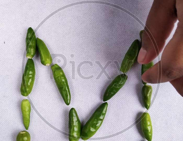 Green Chilli Making "M" Shape In A White Background