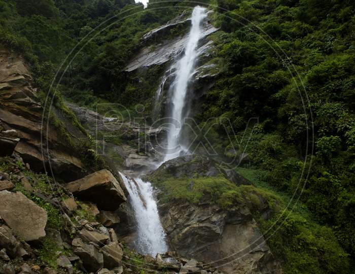 A Water Falls From A High Cliff In A Rocky Forest In Sikkim In India