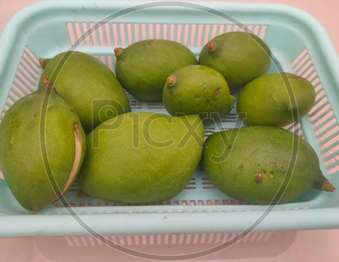 Raw Mangoes On Plastic Basket And Wooden Table Background.