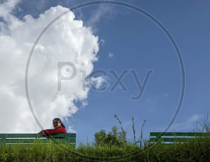 A Beautiful Young Lady In Red Dress Seating On A Green Bench In A Mountain Park In A Sunny Morning
