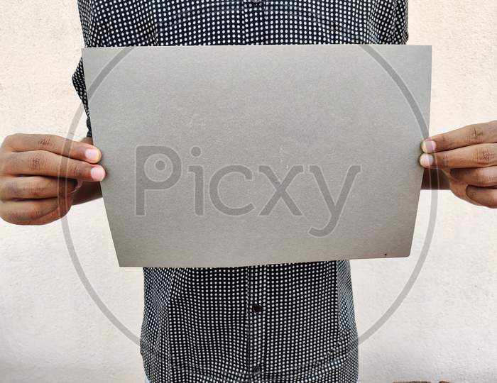 Young Man In Black Shirt Holding A Blank Grey Color Chart Or Board Or Paper. Isolated On White Background.