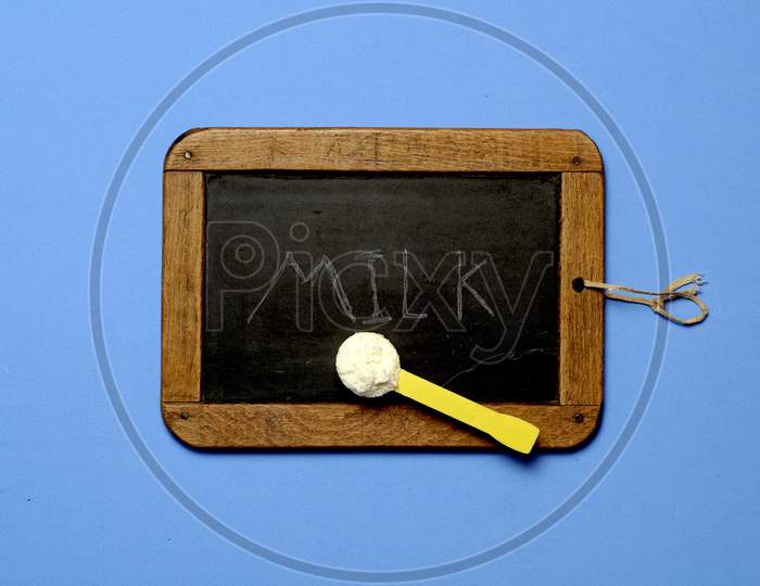 Top View Of Blackboard And Scoop Of Baby Powder Milk With The Word Milk Written On The Blackboard. Flat Lay