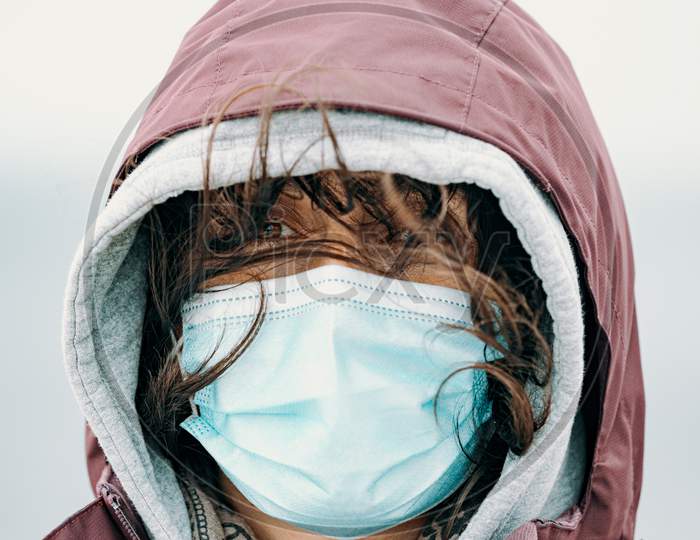 Close Up Of A Woman Face With The Mask Put On And The Hair Flying By The Wind While Wearing Hiking Clothes And Looking Straight To Camera