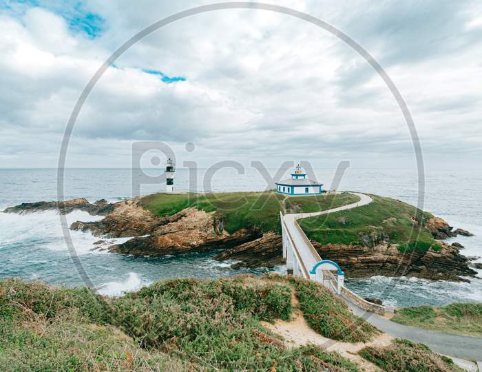 Colorful Shot Of A Lighthouse And A House In A Island In Coruña Spain Over The Wild Ocean