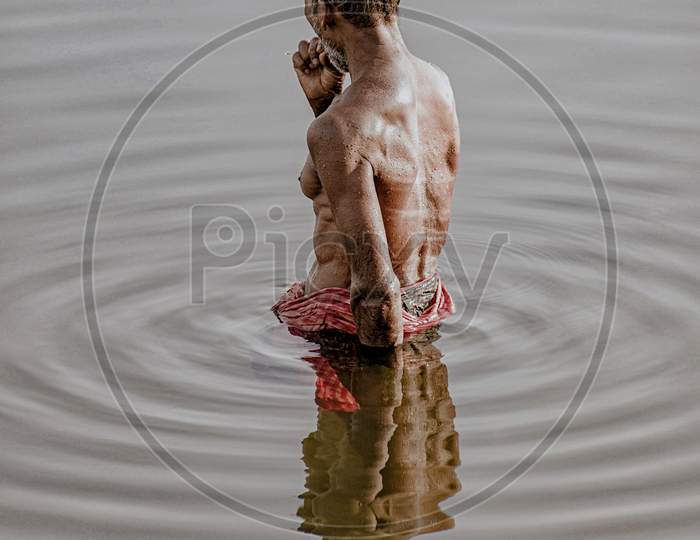 A fit old man bathing in Bindusagar Lake on a hot summer morning.