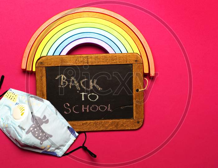Back To School Message Board With Wooden Rainbow And Face Mask. Covid And College Concept. Flat Lay
