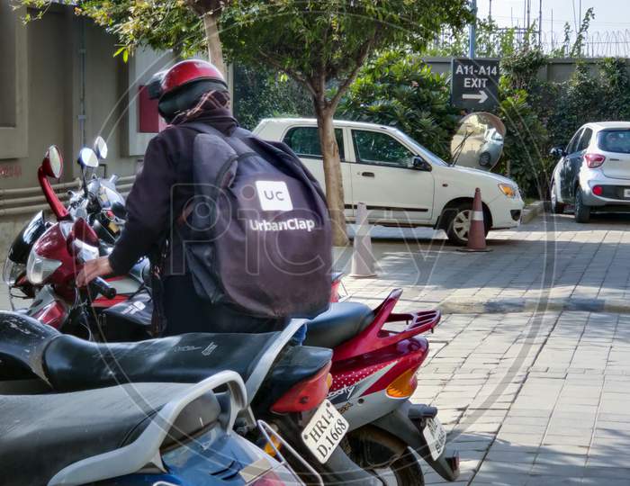 Rider With A Black Urban Clap Urban Company Bag Getting Ready To Sit On A Bike To Deliver Services At Home For The Indian Startup Unicorn