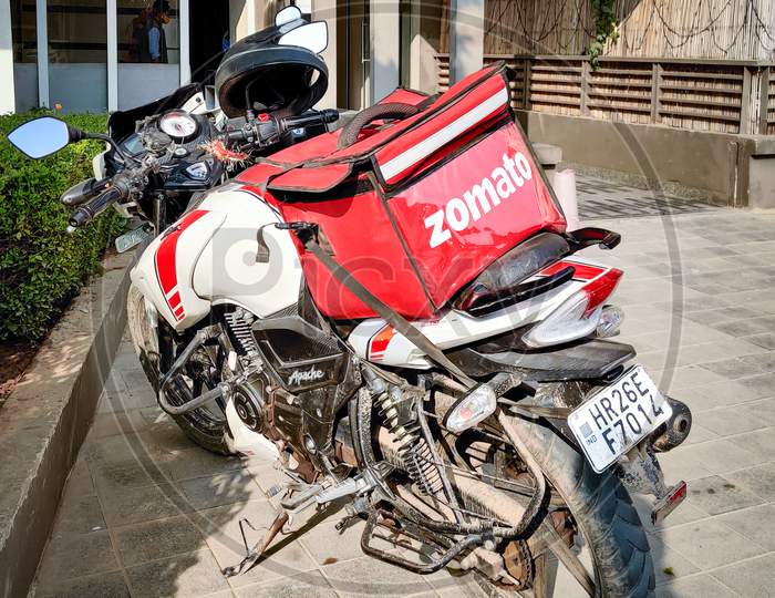 Motorcycle Rider With Red Zomato Bag Delivering Food To A Urban Complex For The Fast Growing Food Tech Startup Unicorn