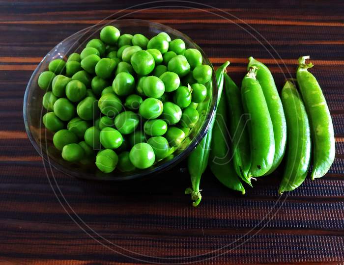 Fresh Green Peas in a Glass Bowl and or with Pea Pods on an Isolated Brown background