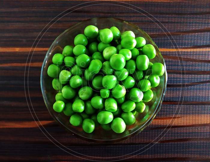 Fresh Green Peas in a Glass Bowl on an Isolated Brown background