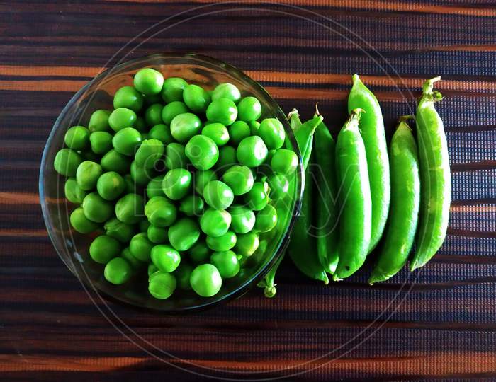 Fresh Green Peas in a Glass Bowl and or with Pea Pods on an Isolated Brown background