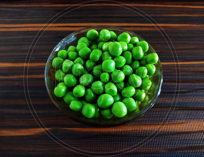 Fresh Green Peas in a Glass Bowl on an Isolated Brown background
