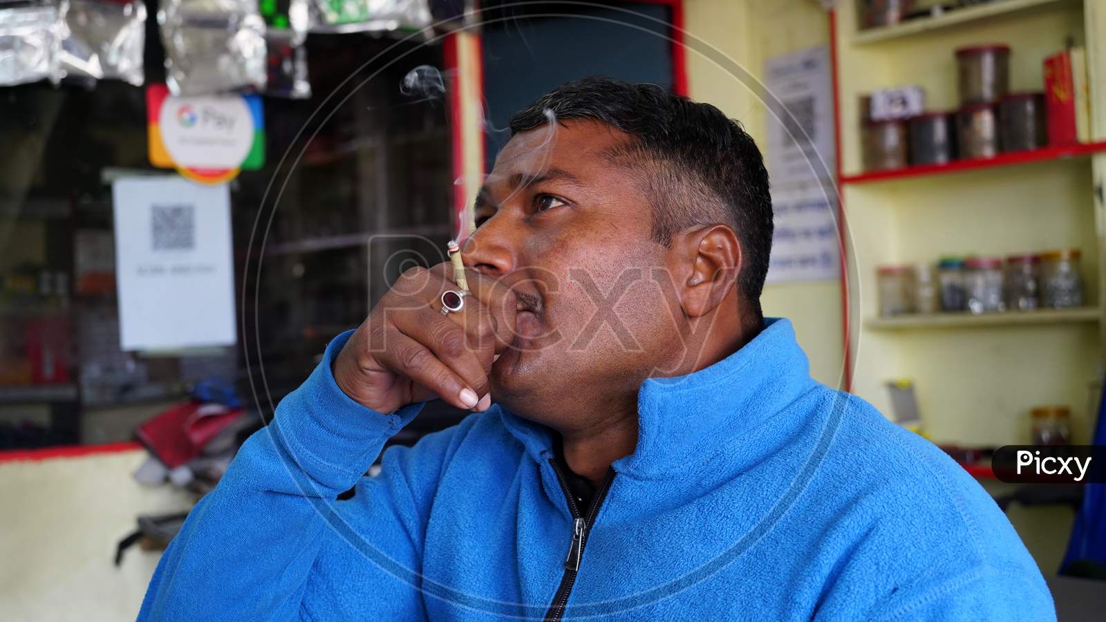 Adult Man Exhales Smoke. Young Inidan Man Holding Traditional Bidi Or Cigarette In Hand.