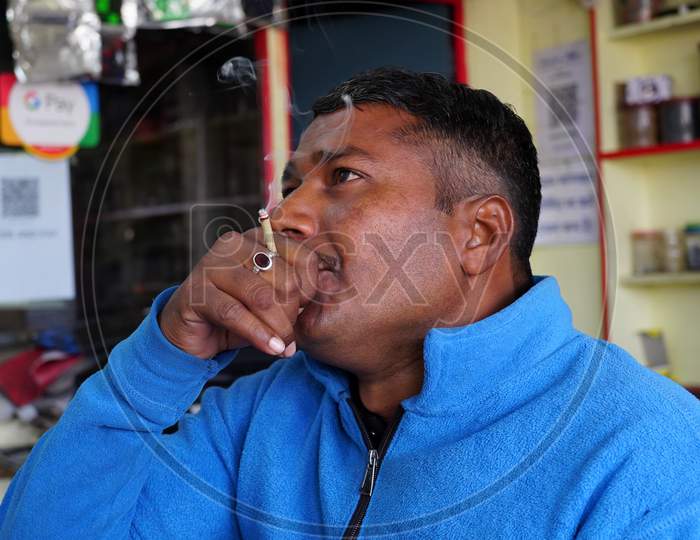 Adult Man Exhales Smoke. Young Inidan Man Holding Traditional Bidi Or Cigarette In Hand.