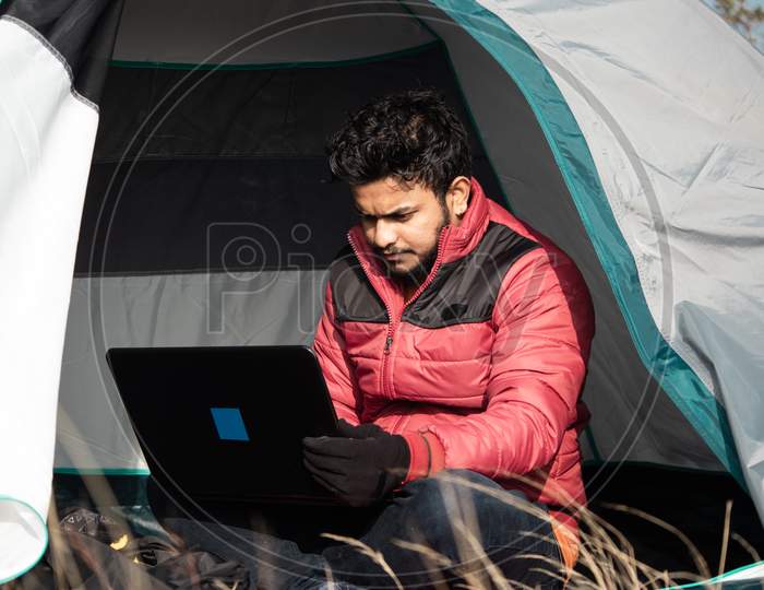 Young Man Busy Working On Laptop Inside The Tent During Camping - Concept Of Digital Nomadic Lifestyle And Solo Travel