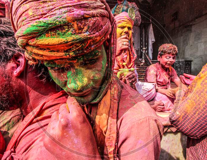 Mathura, Uttar Pradesh/ India- January 6 2020: An Unidentified Men With Face Fully Smeared With Red Color Looks As His Participates In The Holi Celebration At Krishna Temple Looking Down During Holi Festival.