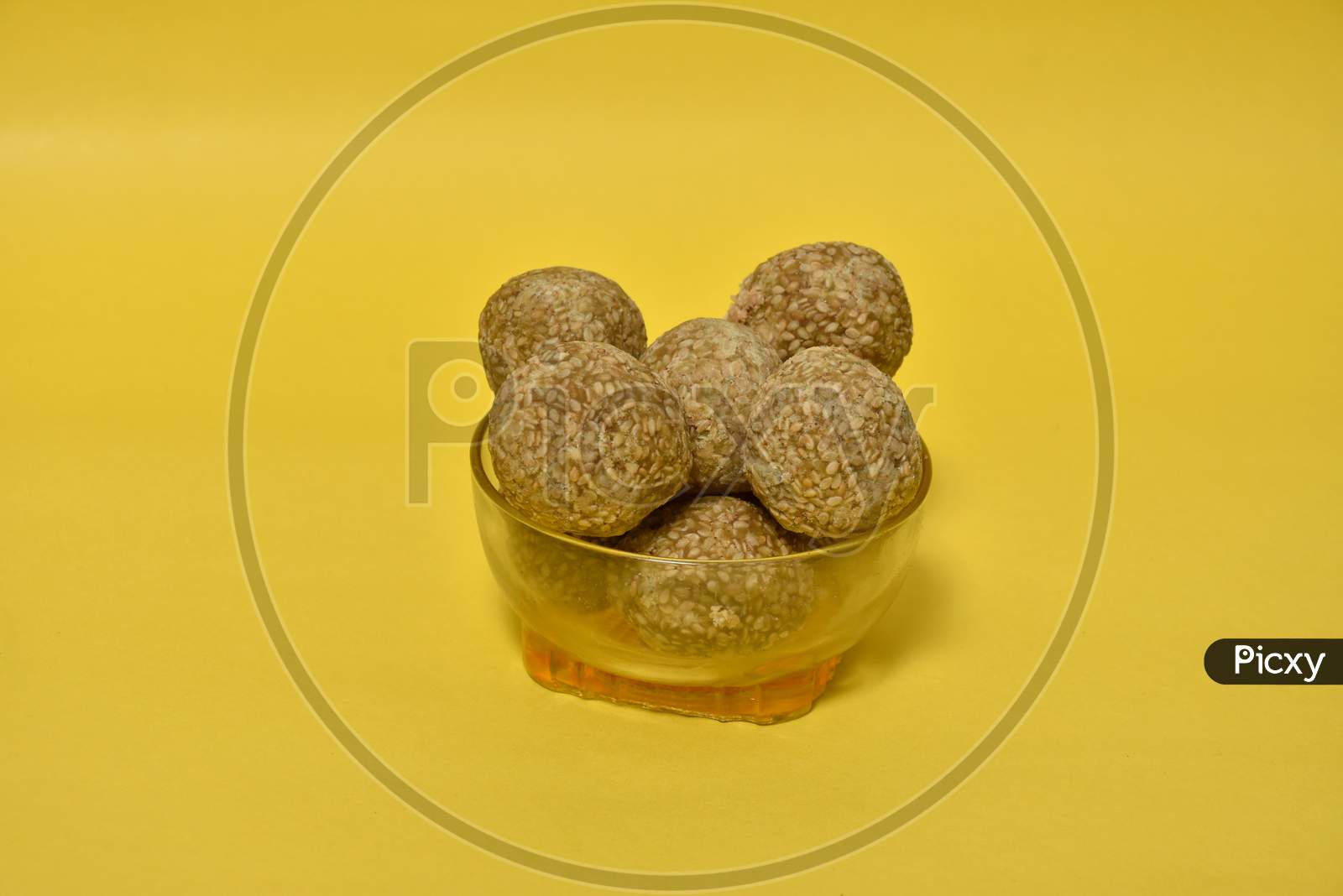Indian sweet Sesame seeds ball or called in Hindi til ke laddu in glass bowl on yellow background.