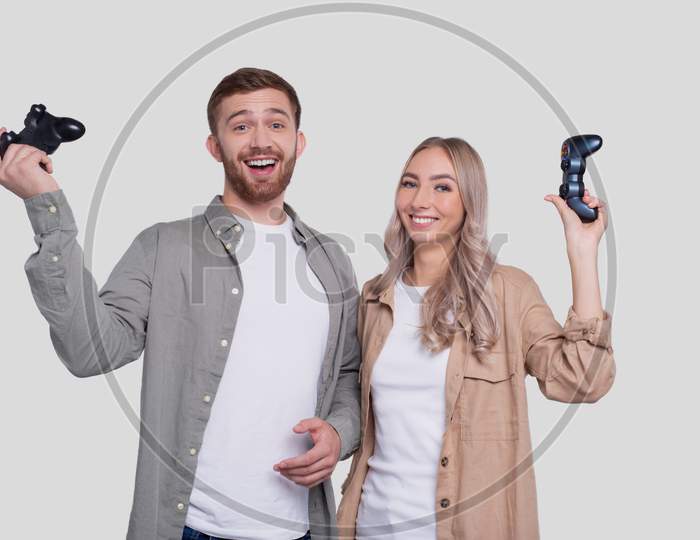 Couple Standing With Joysticks In Hands Smilling Isolated. Happy Couple Playing Console Games.