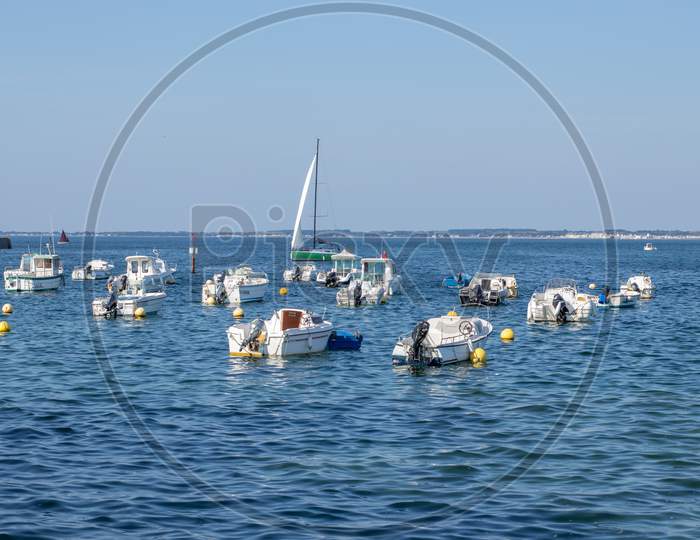 Small White Motor Boats And Sailboats At Anchor In The Blue Dark Water With On The Horizon Beach, Coast, Trees And Sand