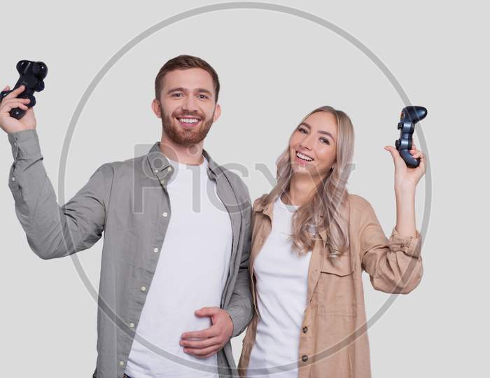 Couple Standing With Joysticks In Hands Smilling Isolated. Happy Couple Playing Console Games.