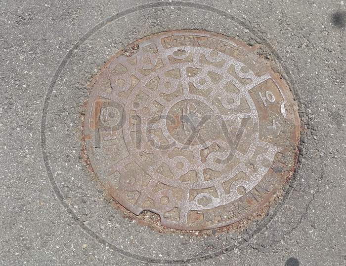 Top View Of A Manhole Cover On Drainage Or Sewerage Under Paved Road.