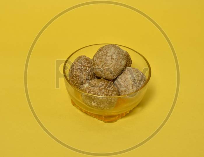 Indian sweet Sesame seeds ball or called in Hindi til ke laddu in glass bowl on yellow background.