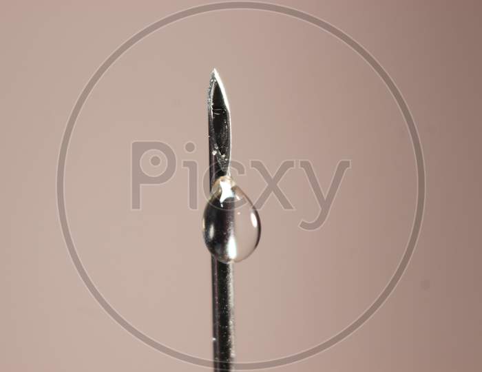 Water Drop Falling From The Syringe Needle Against Grey Background