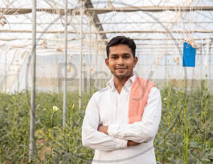 Portrait Of Young Happy Indian Farmer Standing Cross Arms At His Poly House Or Greenhouse, Agriculture Business And Rural Prosperity Concept. Man Wearing White Cloths, Copy Space