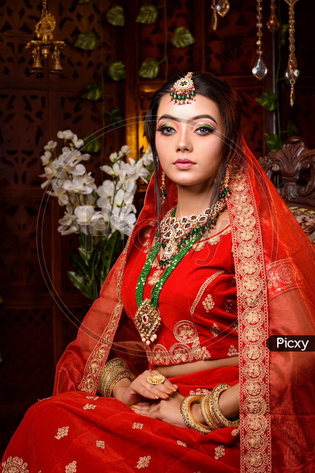 Stunning Indian bride in luxurious bridal costume with makeup and heavy  jewellery is sitting in a chair in with classic vintage interior in studio  lighting. Wedding lifestyle and fashion. Stock Photo