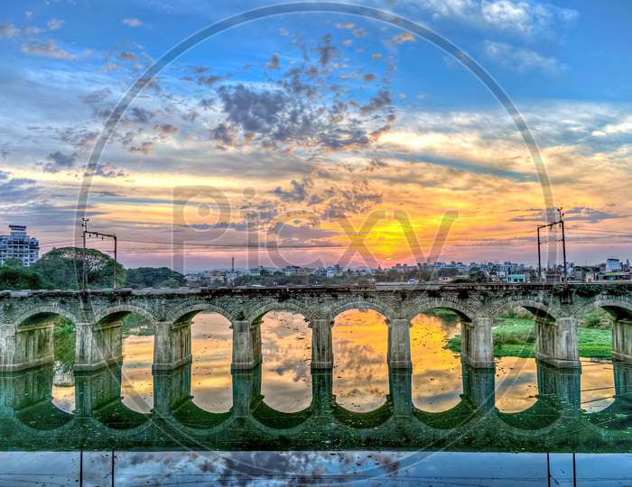 Beautiful Sunset Behind An Old Stone Arched Rail Bridge Reflection And Nice Sky Colors Background.