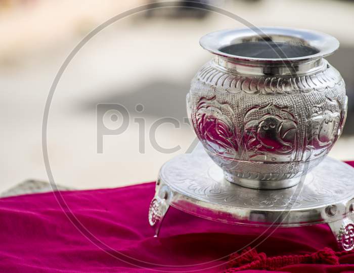 Beautiful Carved Silver Pot Or Kalash And Stand Used In Hindu Rituals, On Blur Background.