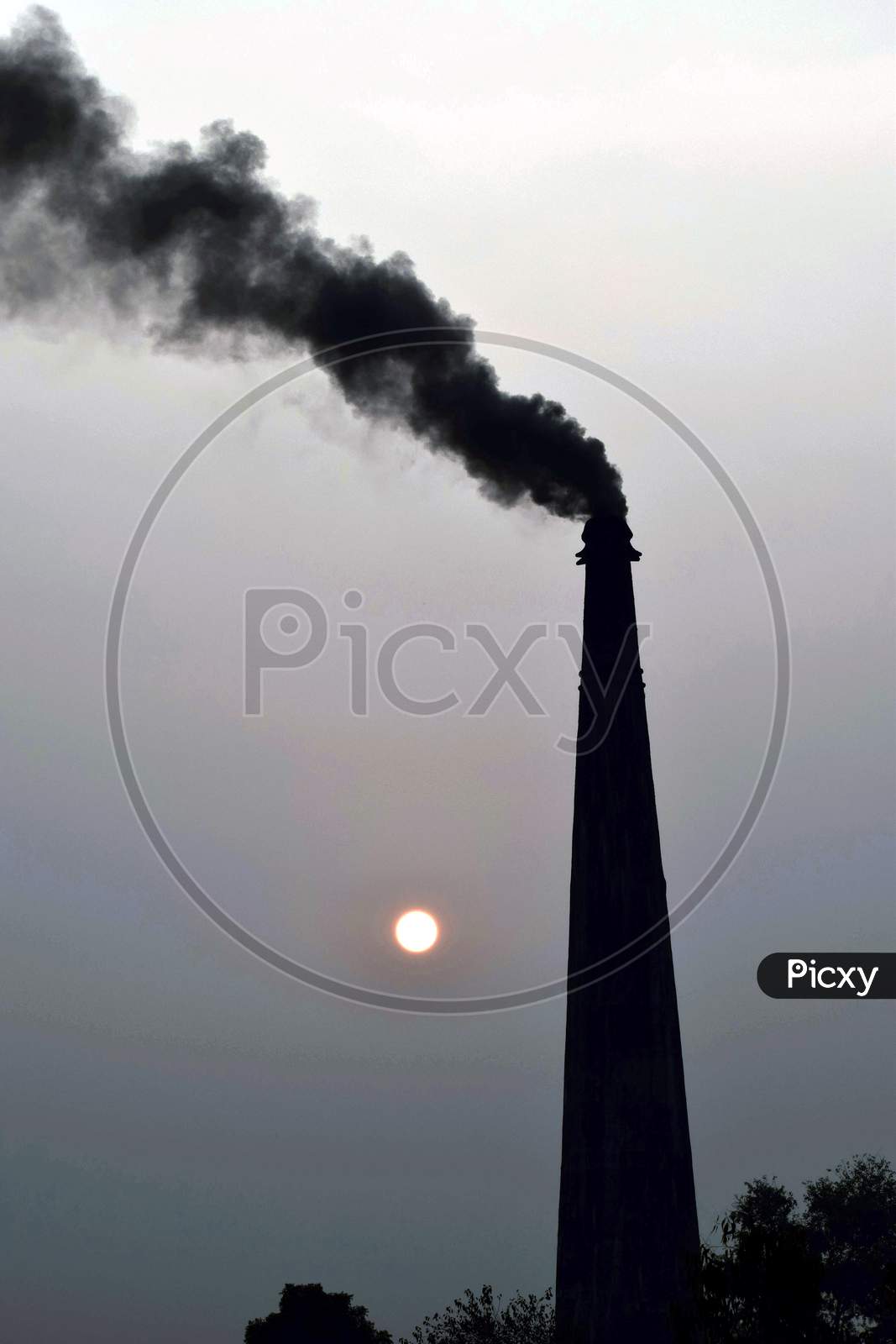 Smoke And Steam Produced Off From The Chimney Against Dark Stormy Sky, Background Sunset