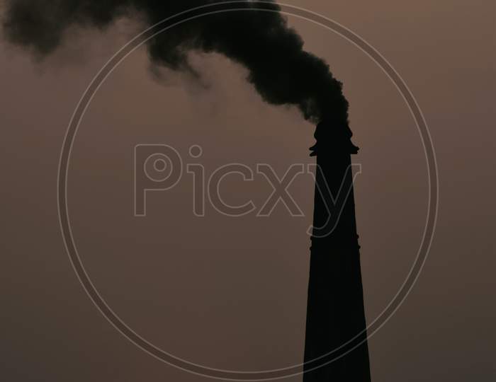 Smoke And Steam Produced Off From The Chimney Against Dark Stormy Sky And Sunset In Background
