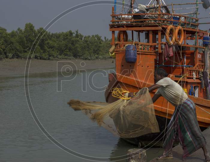 A Fisherman Throwing His Fishing Net At Water For Catching Fish, His Boat Is In Background.