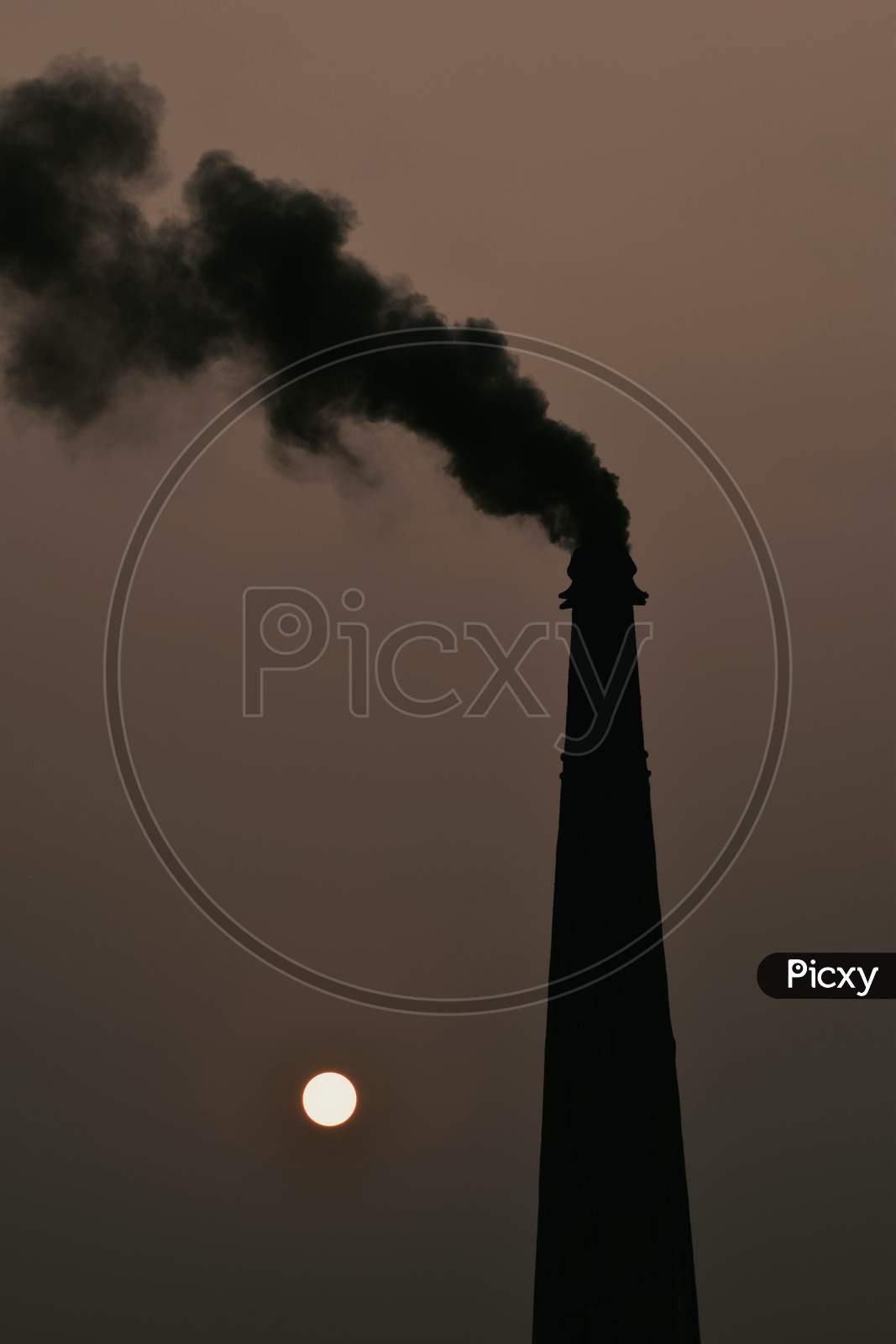 Smoke And Steam Produced Off From The Chimney Against Dark Stormy Sky And Sunset In Background