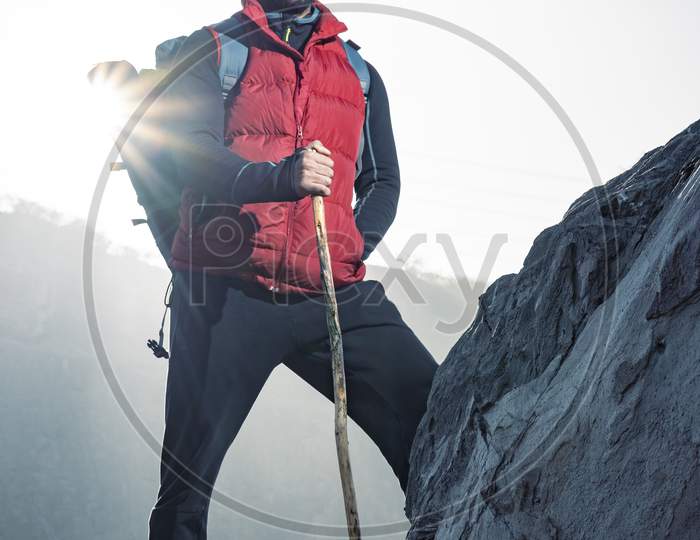 Young Indian Traveler Boy Trekking Over A Rocky Mountain, Standing On The Top Of The Mountain With A Stick In His Hands. Freedom And Adventure Concept.