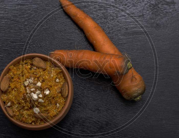 Gajar Ka Halwa Is A Carrot Based Sweet Dessert From India. Garnished With Cashew And Almond Nuts And Served In A Bowl Over Black Background.