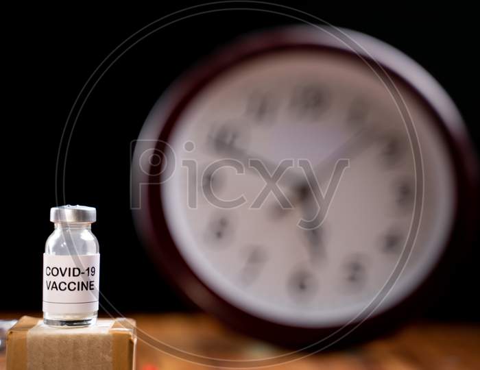 Covid-19 Coronavirus Vaccination Bottle With Clock Behind, Concept Of Covid-19 Vaccine Immunity Duration And Second Dose Time Frame.