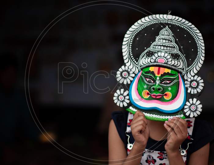 kid girl holding an asian mask by her face and posing angled