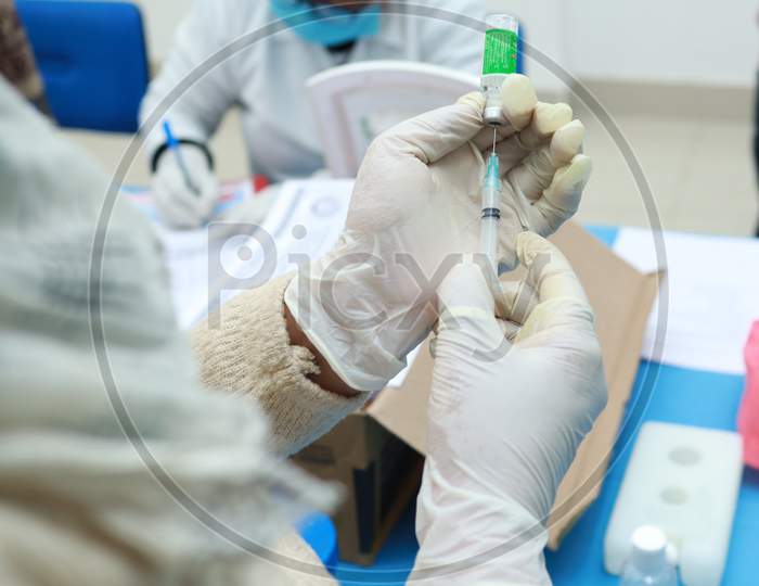A Medical Doctor Drawing Vaccine From A Vial In A Syringe In A Gloved Hand With Selective Focus On Vaccine