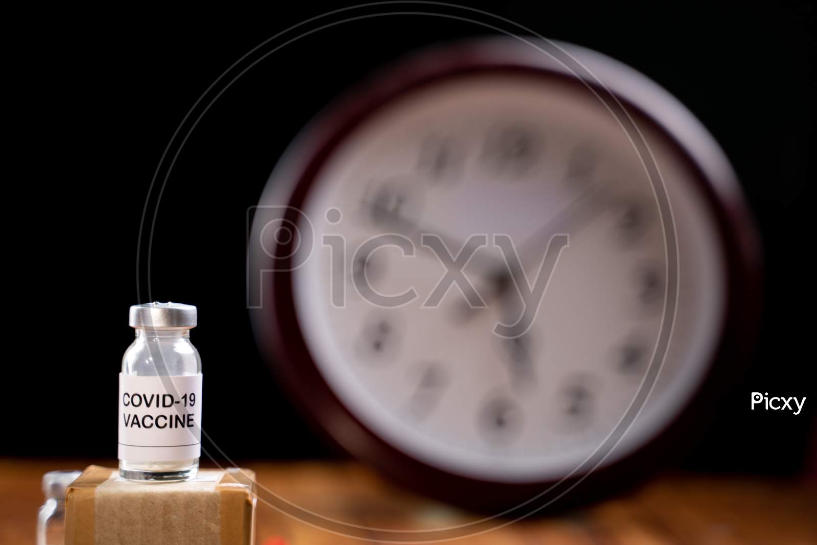 Covid-19 Coronavirus Vaccination Bottle With Clock Behind, Concept Of Covid-19 Vaccine Immunity Duration And Second Dose Time Frame.