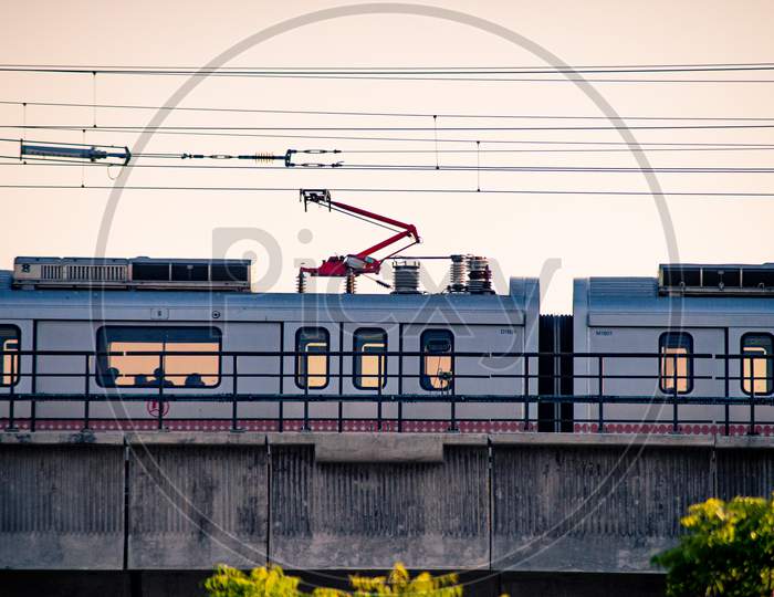 Aerial Dusk Shots Of Metro Train On Elevated Bridge With People Visible Through Transparent Windows And Wires And Support Visible