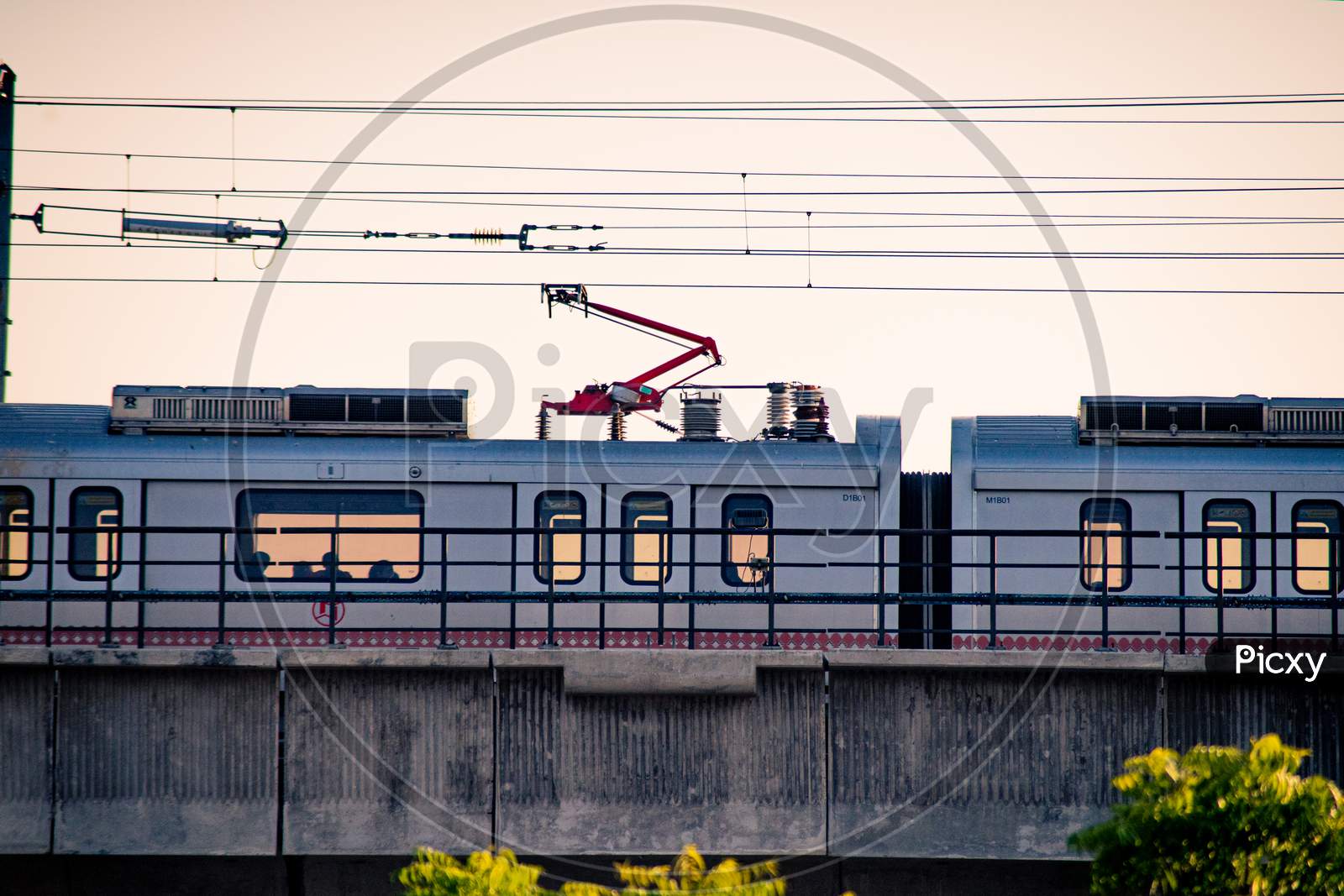 Aerial Dusk Shots Of Metro Train On Elevated Bridge With People Visible Through Transparent Windows And Wires And Support Visible